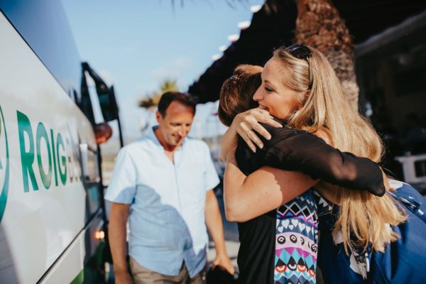 The guests arrive by bus and the bride greets them with a hug.