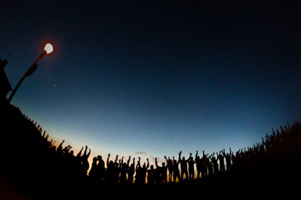 Creative final group photo with all arm lifting guests as a silhouette and the kissing bridal couple against the blue evening sky of Majorca.