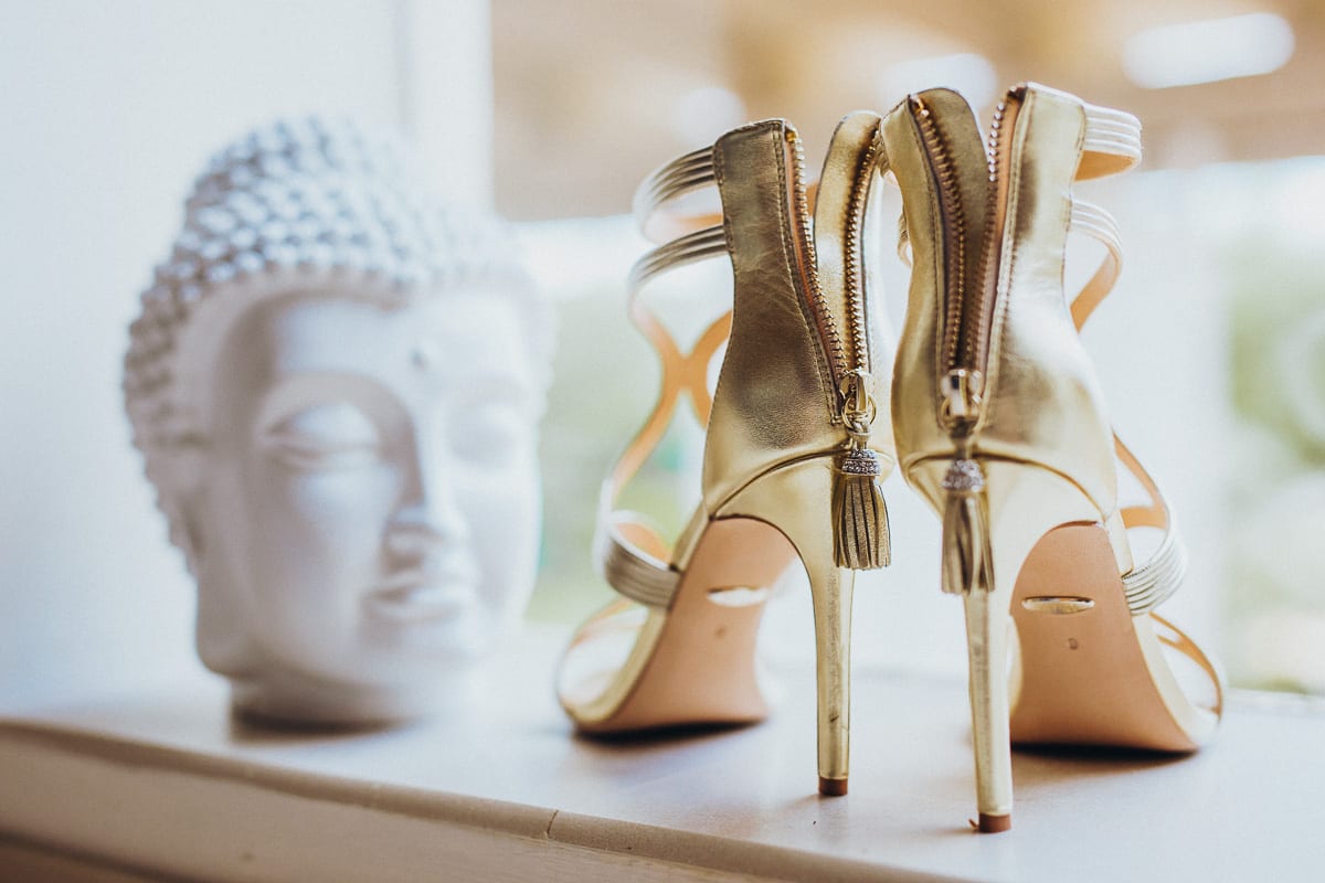 The golden bridal shoes with a white Buddha in the background.