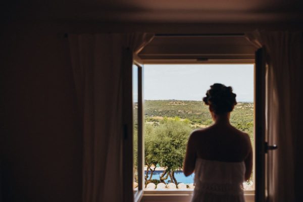 The bride stands by the window and looks into the wide Majorcan landscape.