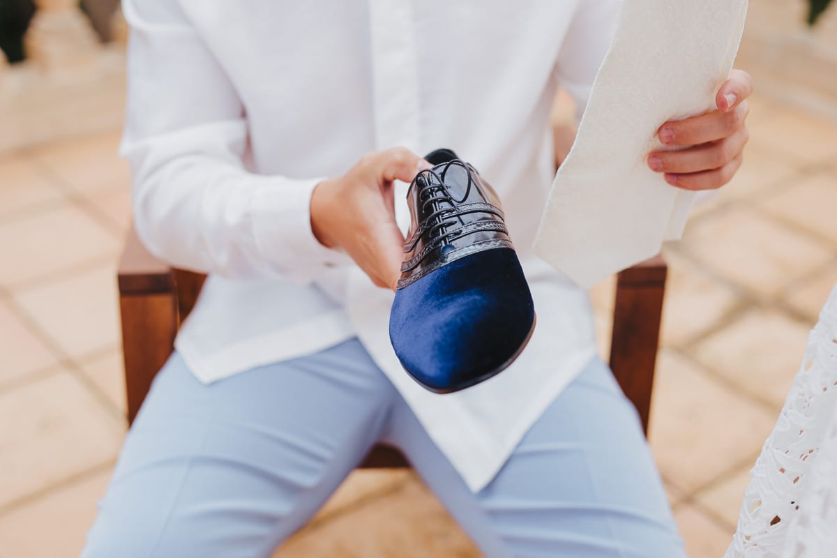 The groom holds one of his shoes in his hand to put it on.