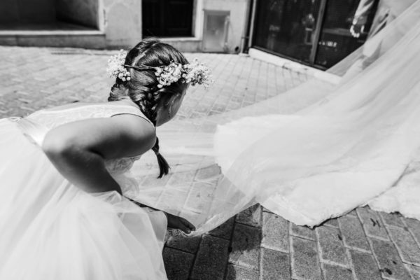 The flower girl turns the veil on the bride while walking.