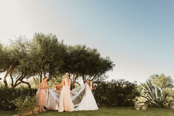 The bridesmaids are straightening the veil of the bride.
