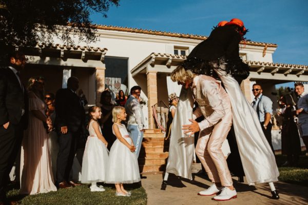 The father of the groom passes laughing through the entertainers on stilts.