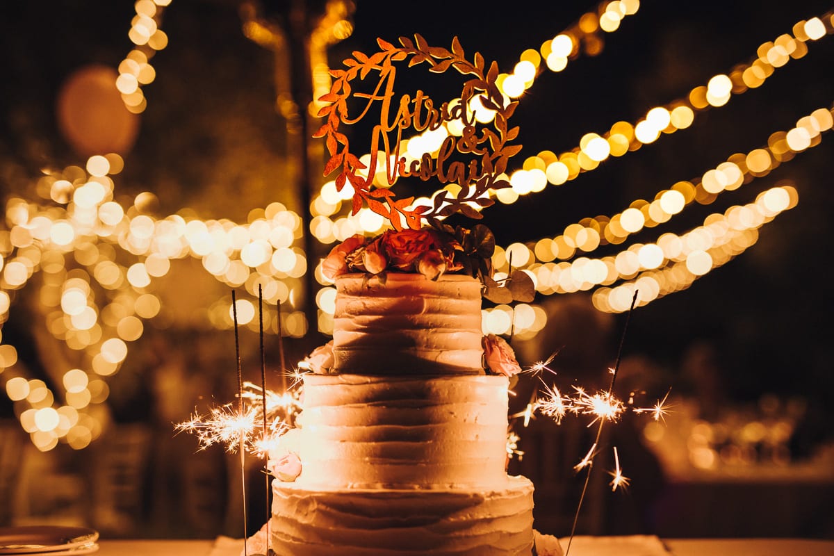 The wedding cake in front of fairy lights with burning sparklers.